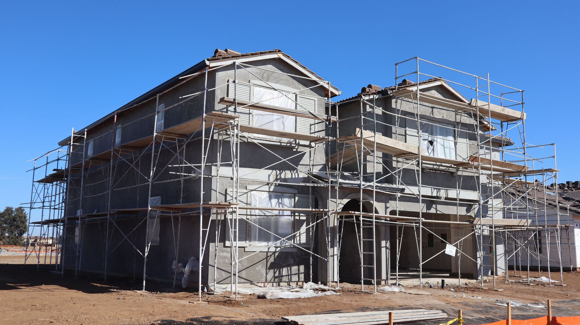A new two-story house under construction with scaffolding on a clear day.